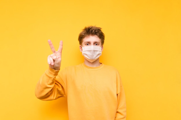 Jovem em uma máscara médica protetora fica em um fundo amarelo olha para a câmera