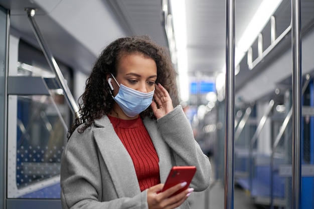 Jovem em uma máscara protetora lendo uma mensagem de texto em um vagão de metrô