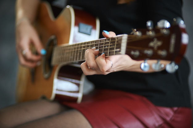 jovem em uma minissaia de couro vermelho e meia-calça preta tocando violão