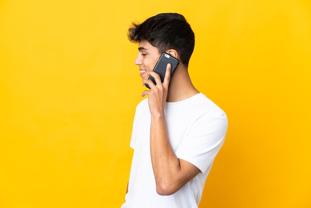 Jovem em uma parede amarela isolada, conversando com alguém ao telefone celular