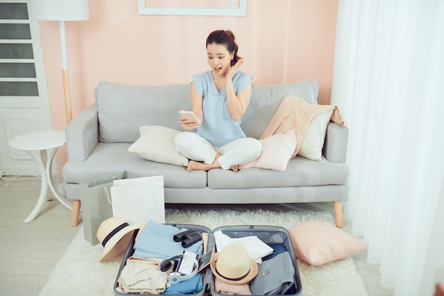 Jovem embalando pertences pessoais em uma mala para viajar sentado no sofá