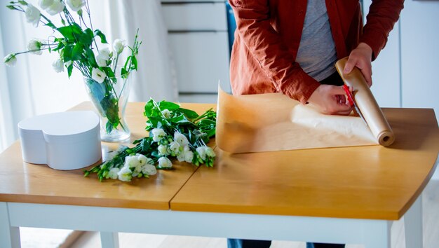 Jovem embrulhando rosas vermelhas em uma mesa na cozinha. Conceito de negócio próprio