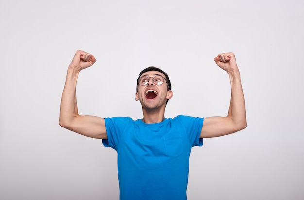 Jovem emocional em roupas casuais, gritando com os braços erguidos, comemorando a vitória, a felicidade e a sorte.