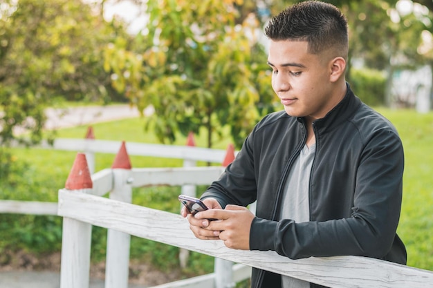 Jovem empreendedor ao lado da cerca de madeira branca com o celular nas mãos