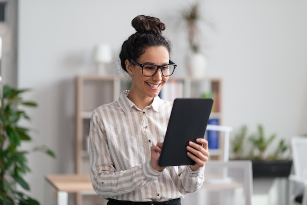 Foto jovem empreendedora positiva usando tablet digital no escritório e sorrindo verificando sua agenda em