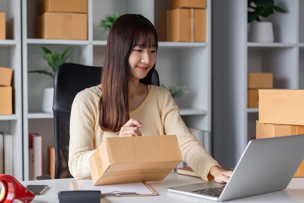 Jovem empreendedora que trabalha em casa vendendo produtos on-line cercada de caixas e usando laptop