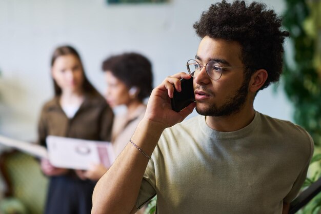 Jovem empregado confiante de óculos e camiseta a falar ao telemóvel