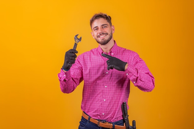 Foto jovem empreiteiro segurando uma chave inglesa em fundo amarelo. homem engenheiro segurando a chave de conserto