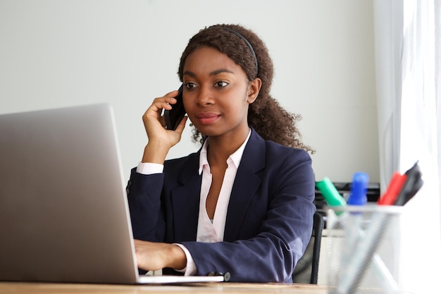 Jovem empresária africana a trabalhar num portátil e a fazer chamadas telefónicas.