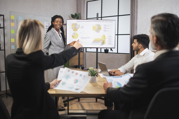 Foto jovem empresária africana confiante mostrando infográficos de trabalho da empresa na tela da parede digital