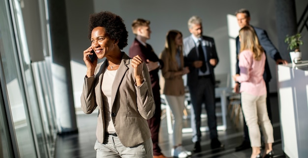 Jovem empresária afro-americana em pé e usando telefone celular em um escritório moderno