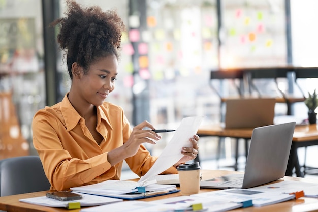 Jovem empresária afro-americana trabalhando na papelada e laptop no espaço de trabalho aberto