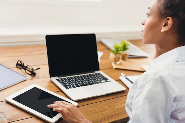 Jovem empresária afro-americana usando laptop com tela em branco, enquanto trabalha em um tablet digital, copie o espaço