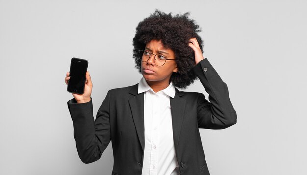 Jovem empresária afro se sentindo perplexa e confusa, coçando a cabeça e olhando para o lado.