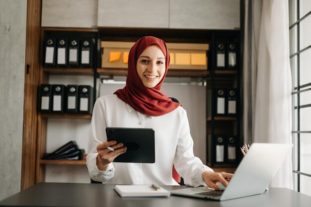 Jovem empresária árabe usando um hijab trabalhando on-line com um laptop no escritório em casa