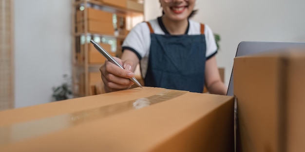 Jovem empresária asiática a trabalhar num armazém a preparar uma caixa de embalagem de PME para entrega em casa de uma pequena empresa