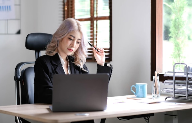 Jovem empresária asiática tem o prazer de ver o trabalho em seu tablet e café favorito no escritório