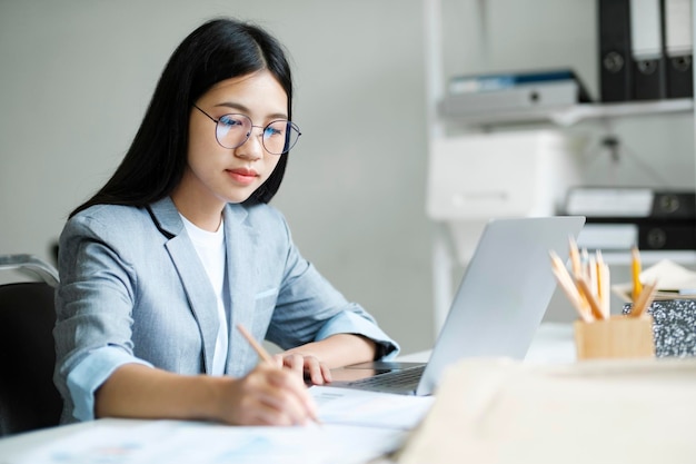 Jovem empresária asiática trabalhando no escritório usando laptop