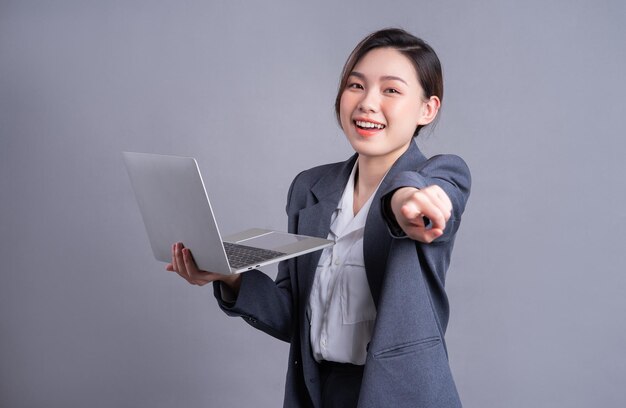 Jovem empresária asiática vestindo terno e usando laptop em fundo cinza