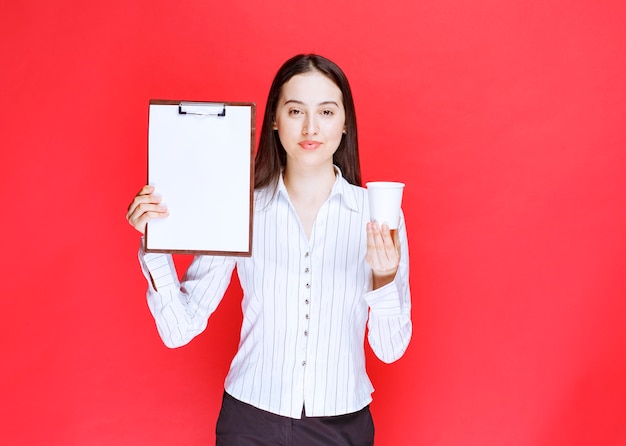 Jovem empresária bonita posando com uma área de transferência vazia e um copo de plástico.