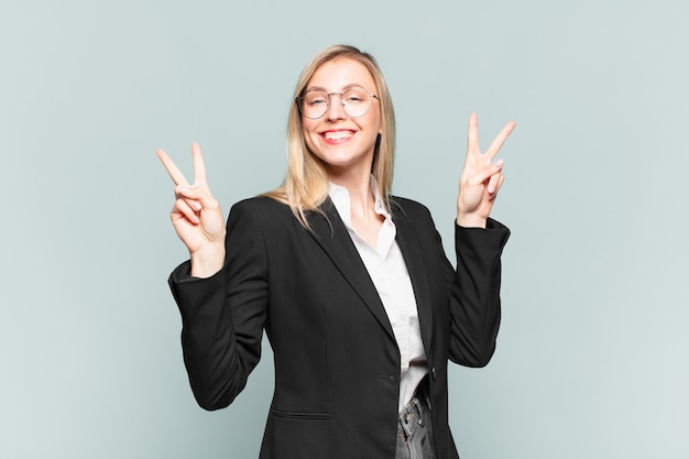 Jovem empresária bonita sorrindo e parecendo feliz, amigável e satisfeita, gesticulando vitória ou paz com as duas mãos