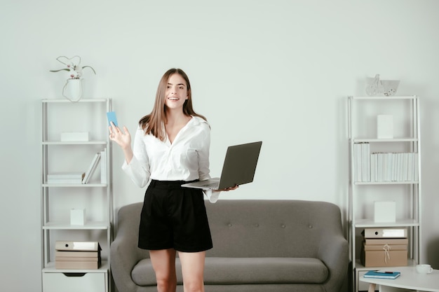 Jovem empresária com laptop e cartão de crédito no local de trabalho no escritório Secretária mulher com roupa formal trabalhando no projeto no escritório moderno