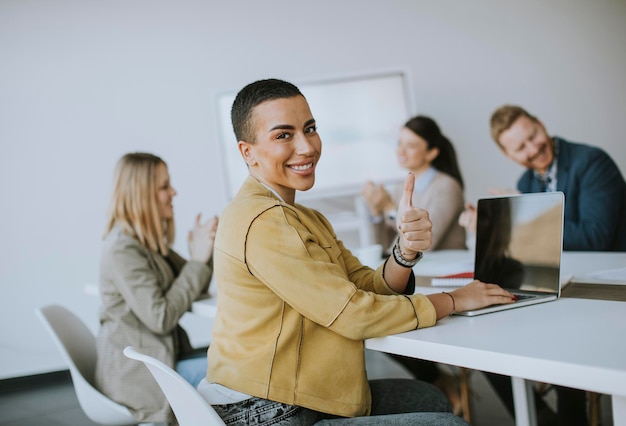 Jovem empresária de cabelo curto sentada no escritório e usando laptop com sua equipe