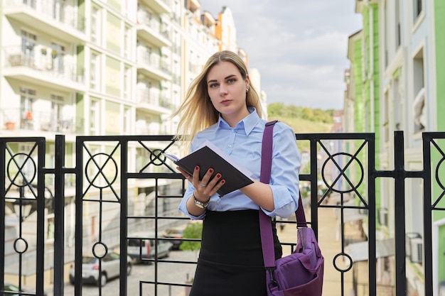 Jovem empresária de camisa azul com bolsa de laptop escrevendo no caderno de negócios