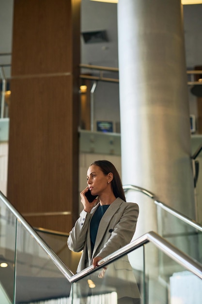 Jovem empresária de pé nas escadas do hotel e conversando ao telefone