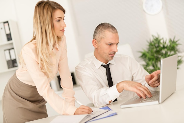 Jovem empresária e empresário trabalhando juntos no laptop no escritório.