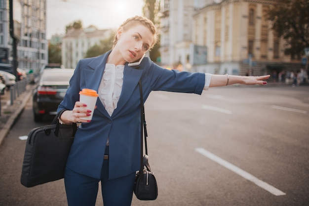 Jovem empresária elegante com uma xícara de café, pegar um táxi