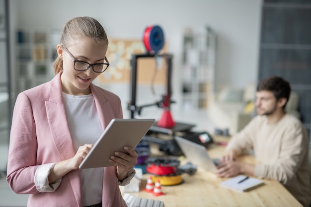 Jovem empresária elegante usando tablet com um colega sentado à mesa em frente ao laptop