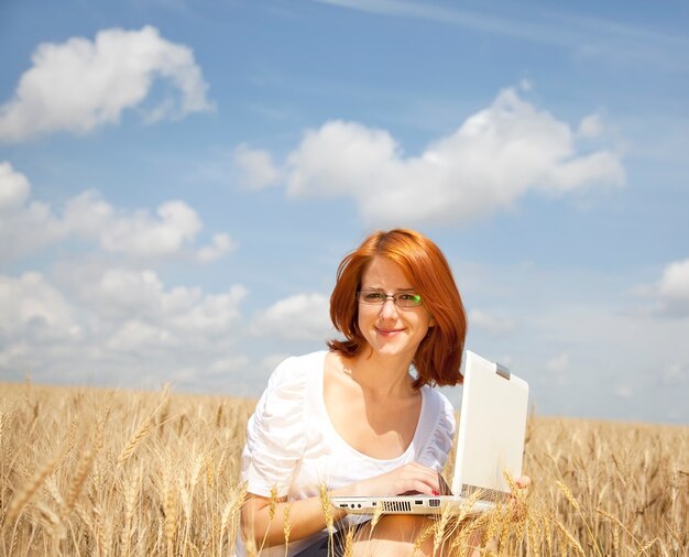 Jovem empresária em branco trabalhando com notebook no campo de trigo.