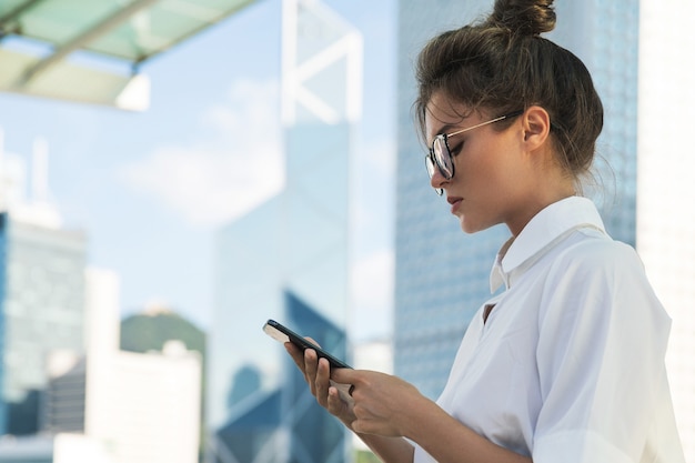 Jovem empresária está usando smartphone na cidade com edifícios modernos