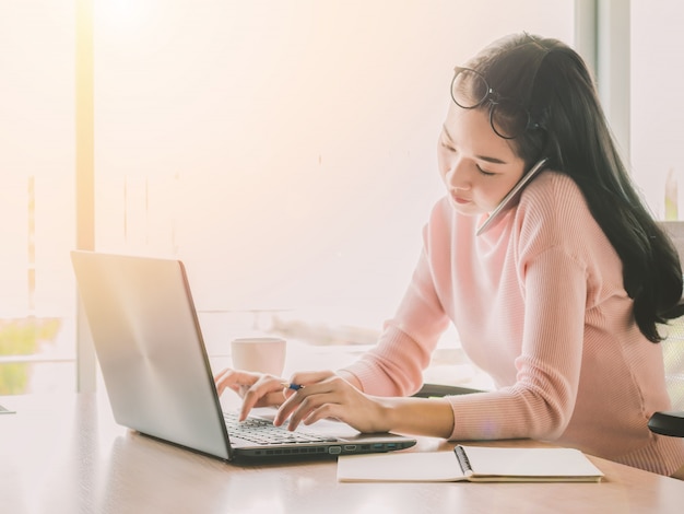 Jovem empresária falando em smartphone e usando laptop