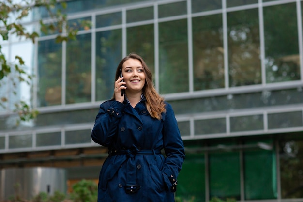 Jovem empresária falando no celular durante a pausa para o café ao ar livre, perto do prédio de escritórios