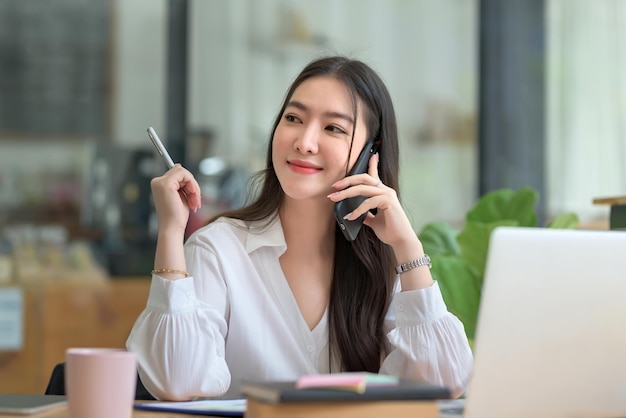 Jovem empresária feliz asiática se comunicando por telefone celular no escritório.