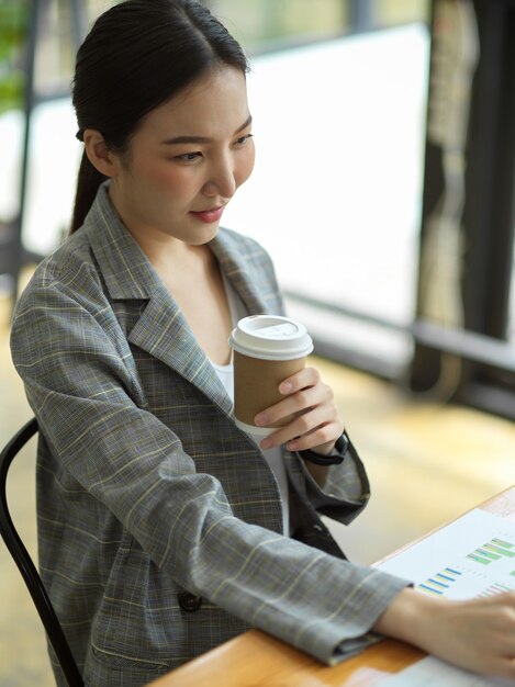 Jovem empresária focada sentar e trabalhar na mesa enquanto bebe café no escritório, trabalhadora de negócios asiáticos trabalhando no laptop