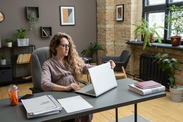 Jovem empresária grávida séria abrindo laptop antes de trabalhar