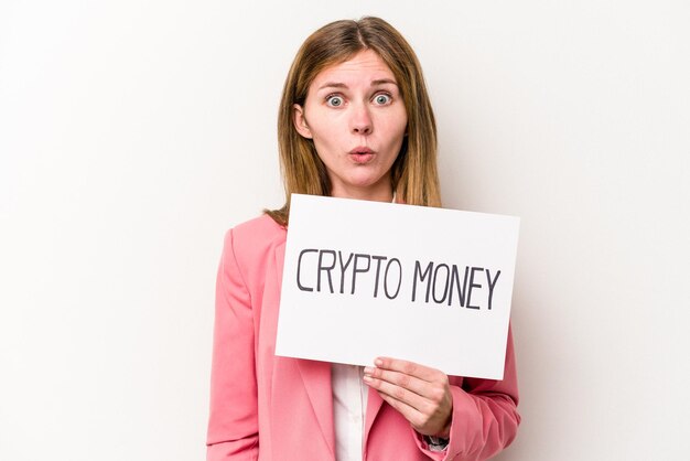 Jovem empresária inglesa segurando um cartaz de dinheiro criptográfico isolado em fundo branco encolhe os ombros e abre os olhos confusos