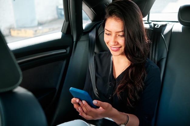 jovem empresária latina usando smartphone no carro