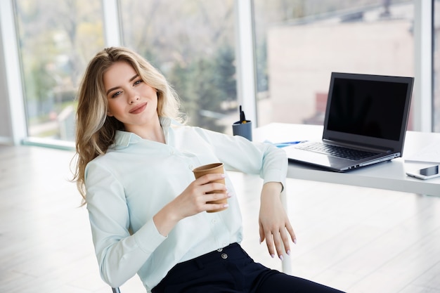 Jovem empresária linda bebe café durante uma pausa no escritório. Conceito de relaxamento