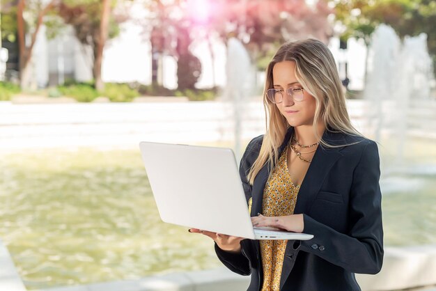 Jovem empresária linda usando óculos usando seu laptop fora do escritório