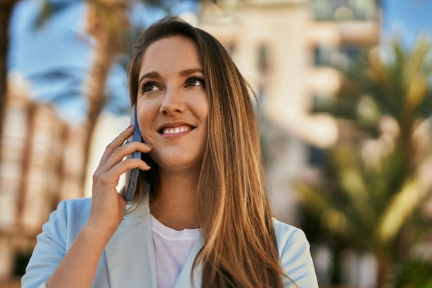 Jovem empresária loira sorrindo feliz falando no smartphone na cidade.