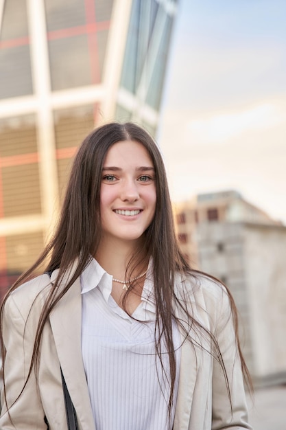 Jovem empresária olhando para a câmera sorrindo com prédio de escritórios em segundo plano