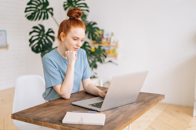 Jovem empresária ruiva bonita digitando no laptop na mesa