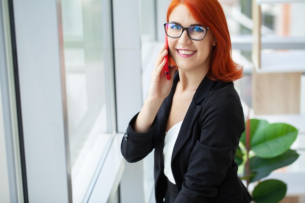 Jovem empresária ruiva com um lindo sorriso em frente a uma janela no escritório