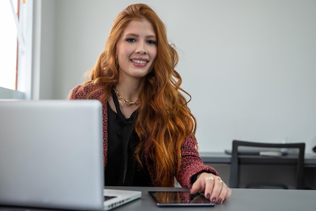 jovem empresária ruiva sentada na frente do computador olhando para a câmera