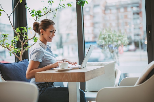 Jovem empresária sorridente em uma pausa em um café. Ela está trabalhando no laptop.