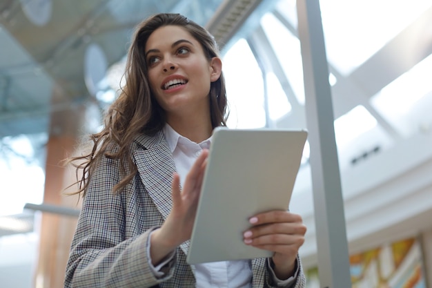 Jovem empresária sorridente no escritório trabalhando em tablet digital.